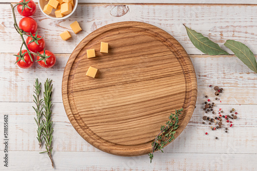 round wooden cutting board with edging. cherry tomatoes, slices of cheese and spices on a white background. mockup with copy space for text, top view
