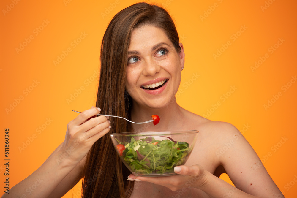 Woman with bare shoulders and long hair eating green salad looking away, isolated portrait on orange yellow background. Woman with bare shoulders and long hair eating green salad looking away, isolated portrait on orange yellow background.