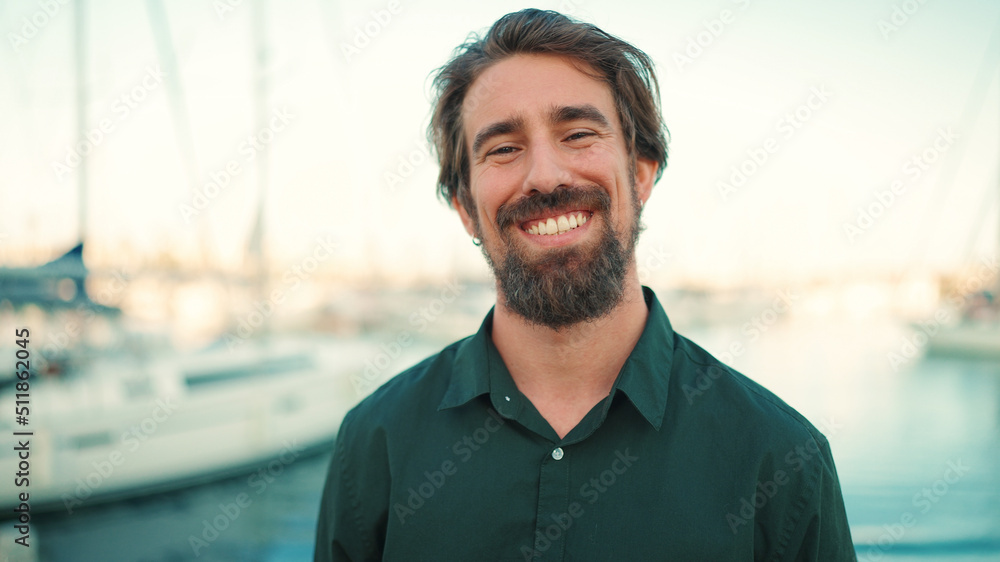 Close-up portrait of a smiling man with a beard on the embankment, on a yacht background. Frontal closeup of happy young hipster male looking at camera Close-up portrait of a smiling man with a beard on the embankment, on a yacht background. Frontal closeup of happy young hipster male looking at camera