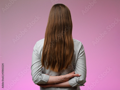 Woman with long hair standing back, isolated on pink.