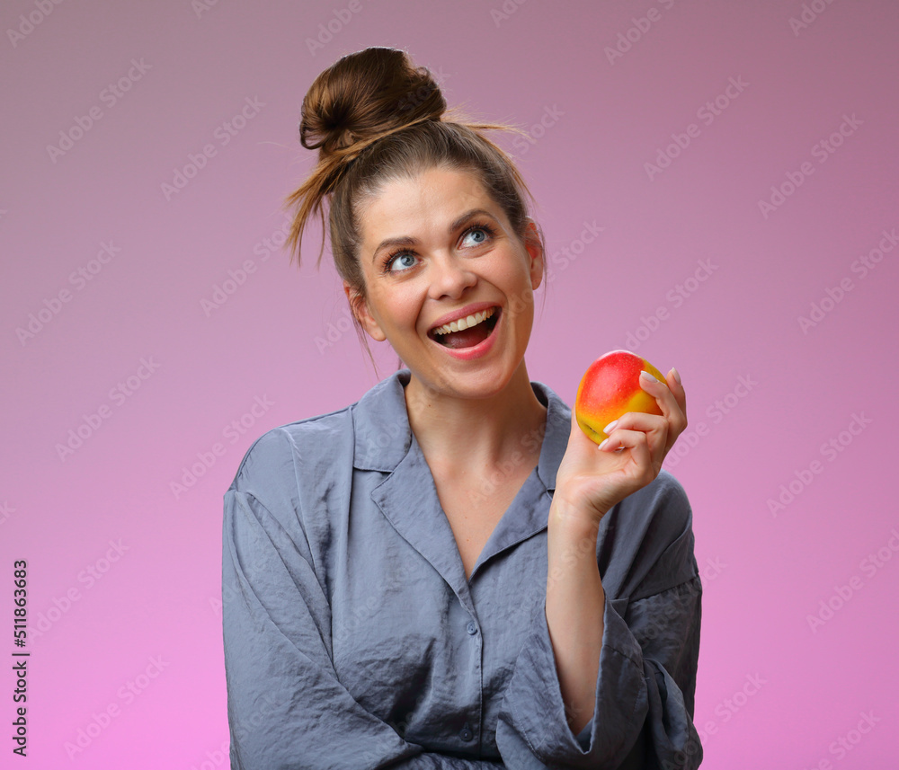 Smiling woman pajama dressed holding apple and looking up, isolated on pink female face portrait Smiling woman pajama dressed holding apple and looking up, isolated on pink female face portrait