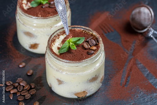 Traditional Italian dessert tiramisu decorated with cocoa powder and green mint in glass jar