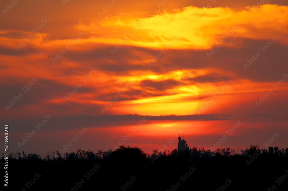 A huge sun on an ominous red sky hangs over a lonely little church by the sea