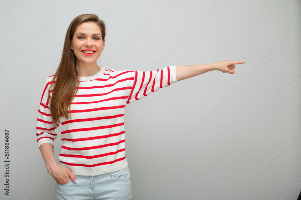 Smiling woman finger pointing to copy space on background, isolated female studio portrait, girl in white sweater with red stripes.. Smiling woman finger pointing to copy space on background, isolated female studio portrait, girl in white sweater with red stripes..