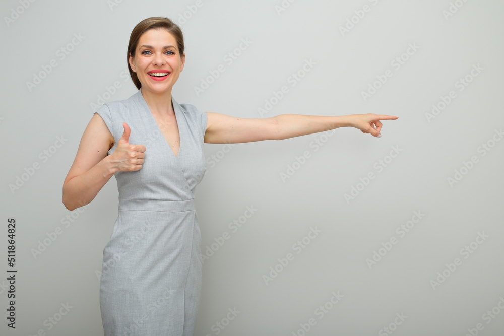Young business woman with short hairstyle finger pointing and keeps thumb up, isolated female studio portrait, young business lady in gray dress. Young business woman with short hairstyle finger pointing and keeps thumb up, isolated female studio portrait, young business lady in gray dress.