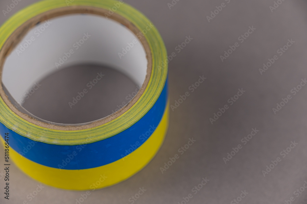 Yellow and blue duct tape. Reel of colored duct tape against the gray background. Selective focus. No people.
