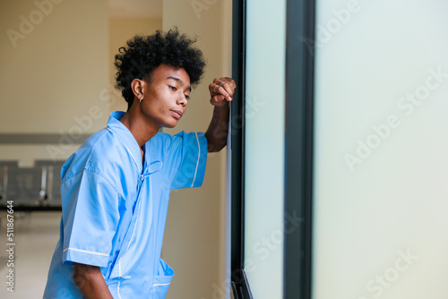 Unhappy lonely depressed and sad feeling. Black man patient standing by windows and look outside at medical center.
