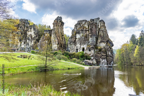 The dog swims in the lake near unique rock formation Externsteine, Germany