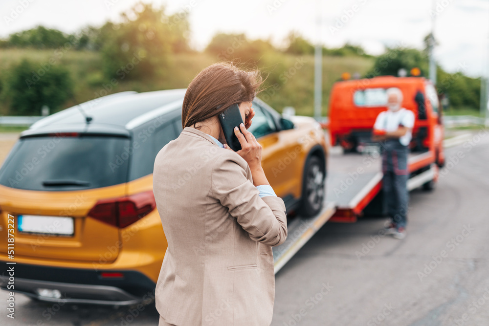 Elegant middle age business woman calling someone while towing service helping her on the road. Roadside assistance concept.