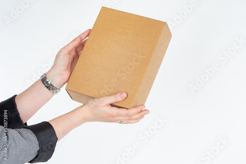 Cardboard box in hand. Women's hands with gift. Box symbolizes gift for holiday. Girl holds out box forward. Concept of giving gift or parcel. Small cardbox without inscriptions. Blank for your logo © Grispb