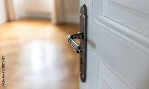 Door open close up. Retro doorknob on white door, blur floor parquet, classy room interior