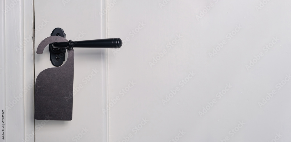 Hotel room hanger blank, empty for your text. Black label on closed door knob, close up view. Hotel room hanger blank, empty for your text. Black label on closed door knob, close up view.
