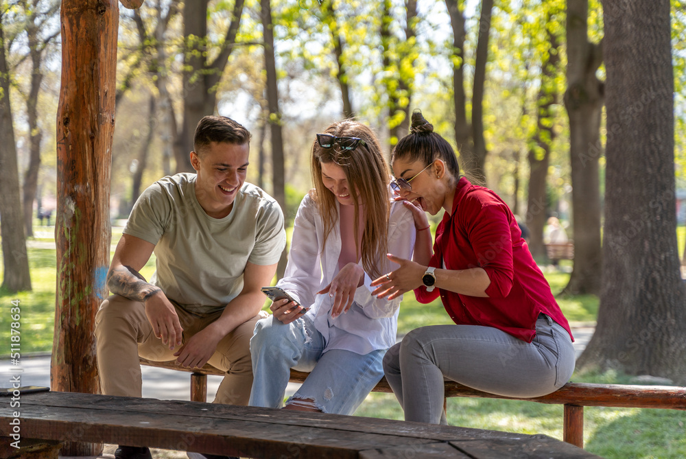 Young people watching online content in a smart phone sitting on a bench