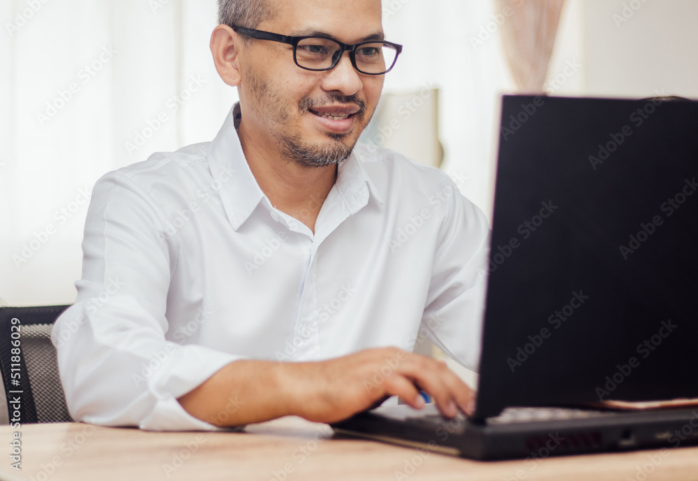 Happy man wearing glasses and smiling as he works on his black laptop where business is going well. Happy man wearing glasses and smiling as he works on his black laptop where business is going well.