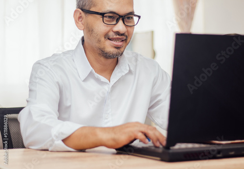 Happy man wearing glasses and smiling as he works on his black laptop where business is going well.