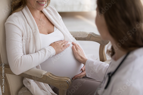 Hand of unknown obstetrician touches big belly of pregnant woman during visit at home, close up cropped shot. Prenatal care, doula consults future mother, pregnancy, motherhood and medicine concept photo