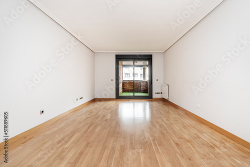 Empty living room with oak parquet and dark aluminum window leading to open terrace with green floor