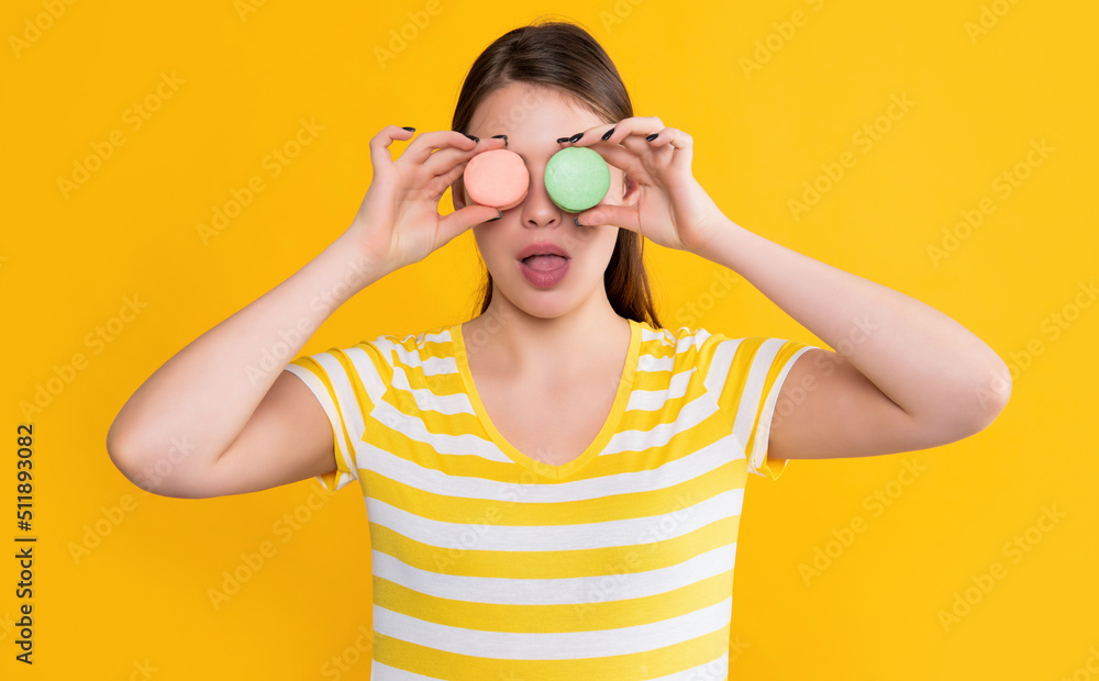 surprised young girl with macaron on yellow background surprised young girl with macaron on yellow background