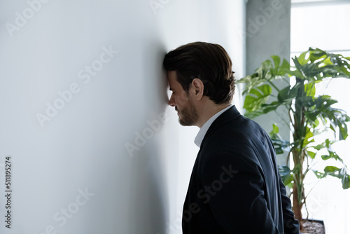 Photographie Upset businessman banging his head against wall in despair looks stressed having
