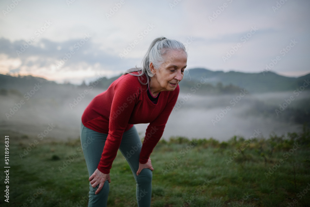 Obraz premium Senior woman doing breathing exercise in nature on early morning with fog and mountains in background.