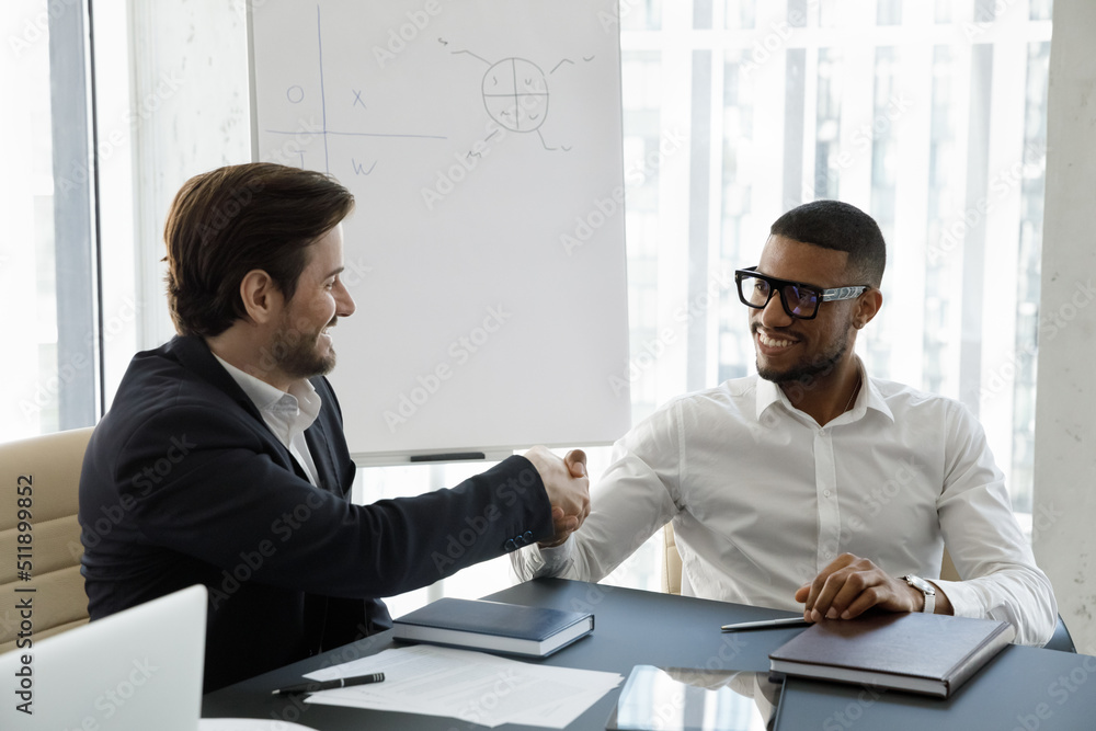 Multi ethnic business partners succeed goal finish formal appointment in office shaking hands feeling satisfied by meeting result. Accomplish negotiations successfully make deal partnership concept Ph...