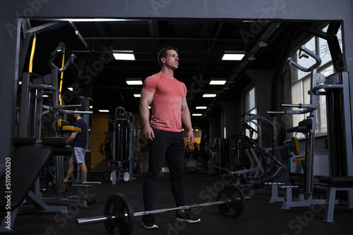 Strong muscular sportsman looking focused, standing in front of heavy barbell