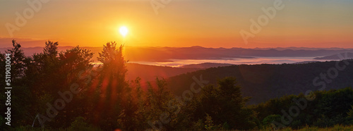 Panorama of a beautiful sunrise in the mountains. White morning mist swirls in the valley © Rejdan