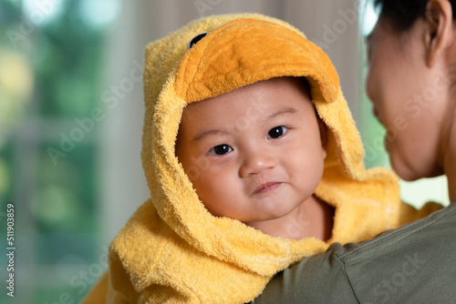 Happy Asian baby smile and laughing wearing yellow duck shower cloth in mother arms. Bathing time. Adorable baby looking at camera waiting to washing and bathing. Baby care concept