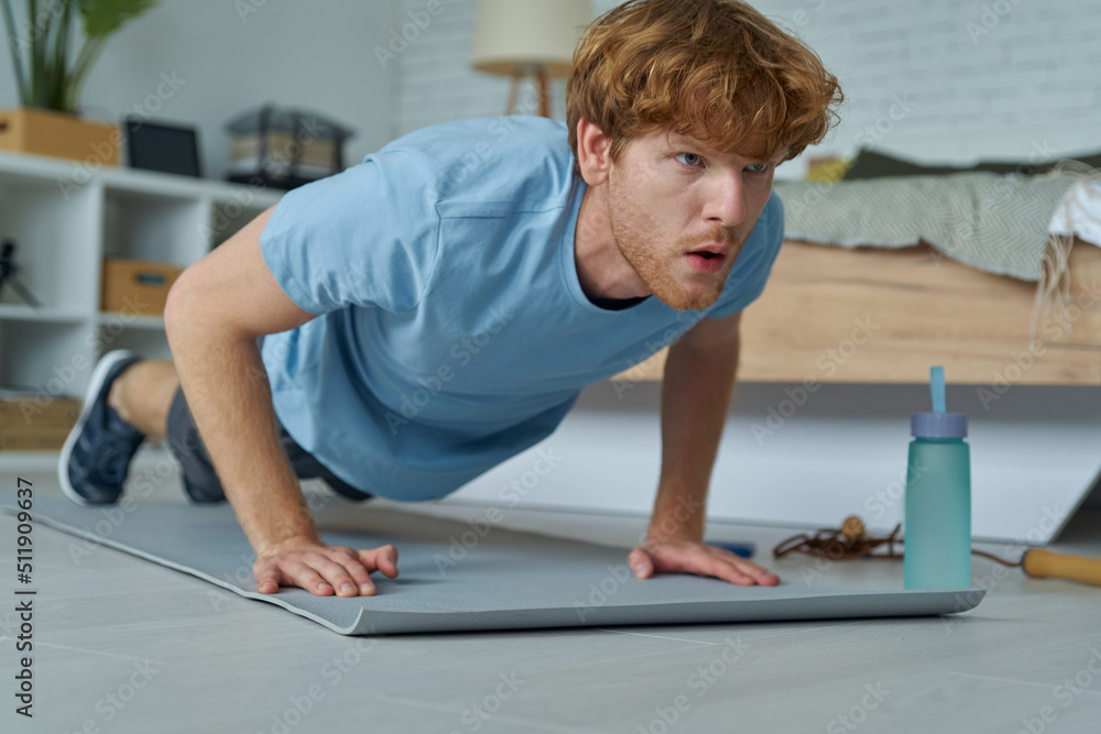 Confident young redhead man doing push-ups at home Confident young redhead man doing push-ups at home