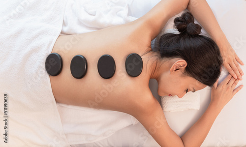 Beautiful young woman relaxing in spa salon with hot stone massage on body. Beauty treatment therapy.