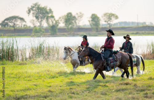 Group of cowboy control horse to walk through grass field cover by water near river and show some splash during walking.