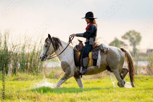 One cowboy with hat control horse to walk through grass field cover by water near river and show some splash during walking.