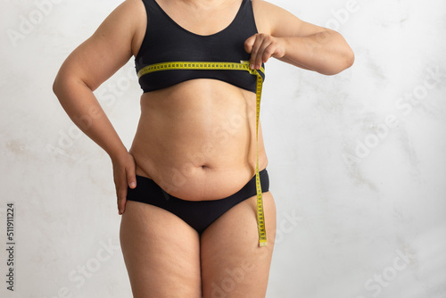 Unrecognizable naked overweight woman in underwear, hold and measuring by roulette tape her breast, chest. Disproportion of body, health care, home cellulite treatment. White isolated background