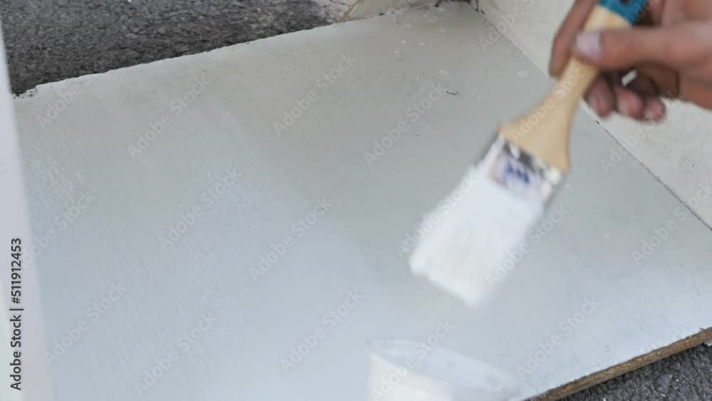 painter's hand paints plywood shelving with white paint on the second