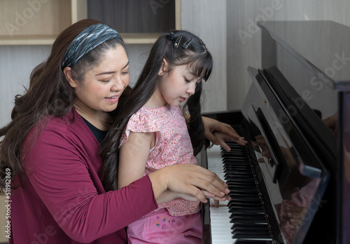 Girl learning piano with teacher woman at home. Asian pianist teacher teaching girl kid student to play piano at school.