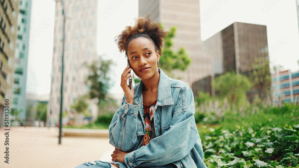 Beautiful African girl with ponytail wearing denim jacket talking on mobile phone on modern city background. Beautiful African girl with ponytail wearing denim jacket talking on mobile phone on modern city background.