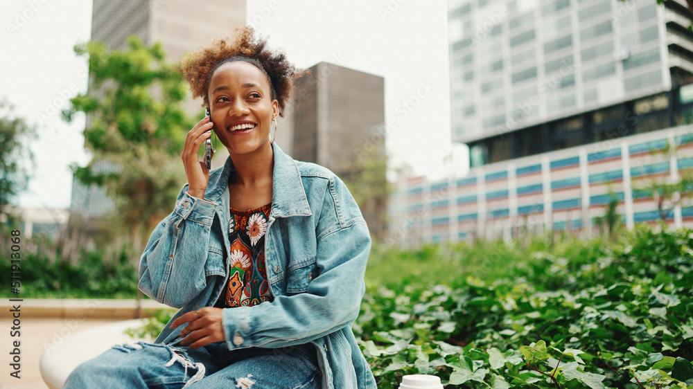 Beautiful African girl with ponytail wearing denim jacket talking on mobile phone on modern city background. Beautiful African girl with ponytail wearing denim jacket talking on mobile phone on modern city background.