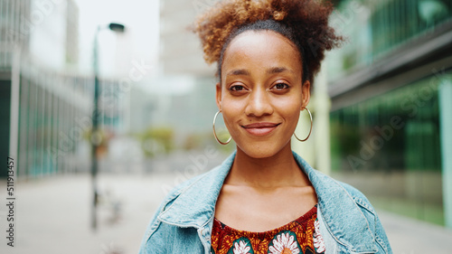 Frontal portrait of an African girl with ponytail  wearing denim jacket  in crop top with national pattern with smile looking at the camera.