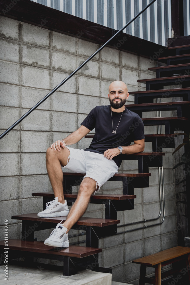 Naklejka premium A young man in t-shirt and shorts on the stairs at city streets