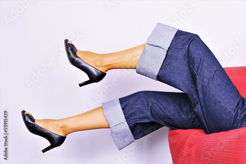 Woman legs wearing wide leg dark blue jeans trouser lie down on red sofa. photo isolate on white background
