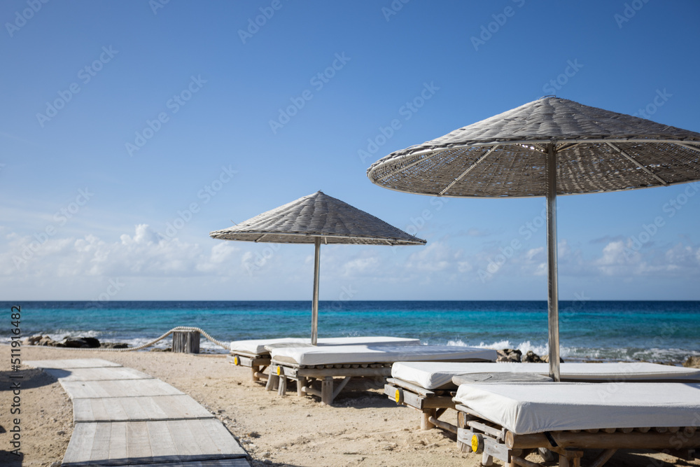 Wooden sun loungers with sun umbrellas on a tropical beach.