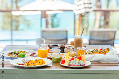Delicious breakfast set on wooden table next to the pool with sea view. Morning food in tropical modern resort. Assortment of fresh food - fruits, vegan juices, matcha green tea and pastry
