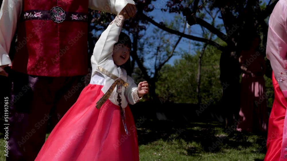 Korean family in national costumes in nature stands next to a cherry blossoming tree Korean family in national costumes in nature stands next to a cherry blossoming tree