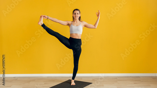 Fototapeta Naklejka Na Ścianę i Meble -  Beautiful young woman practicing yoga indoors. Utthita Hasta Padangusthasana, Extended Hand to Big Toe pose. Yellow background. Web banner
