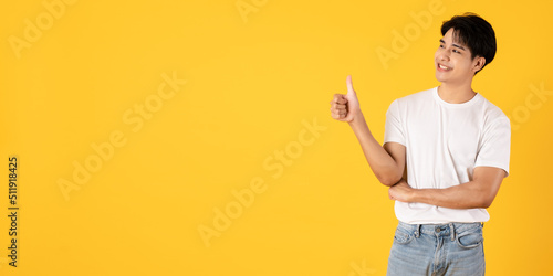 Smiling young asian teenage man wearing white shirt and jeans on yellow background giving thumbs up
