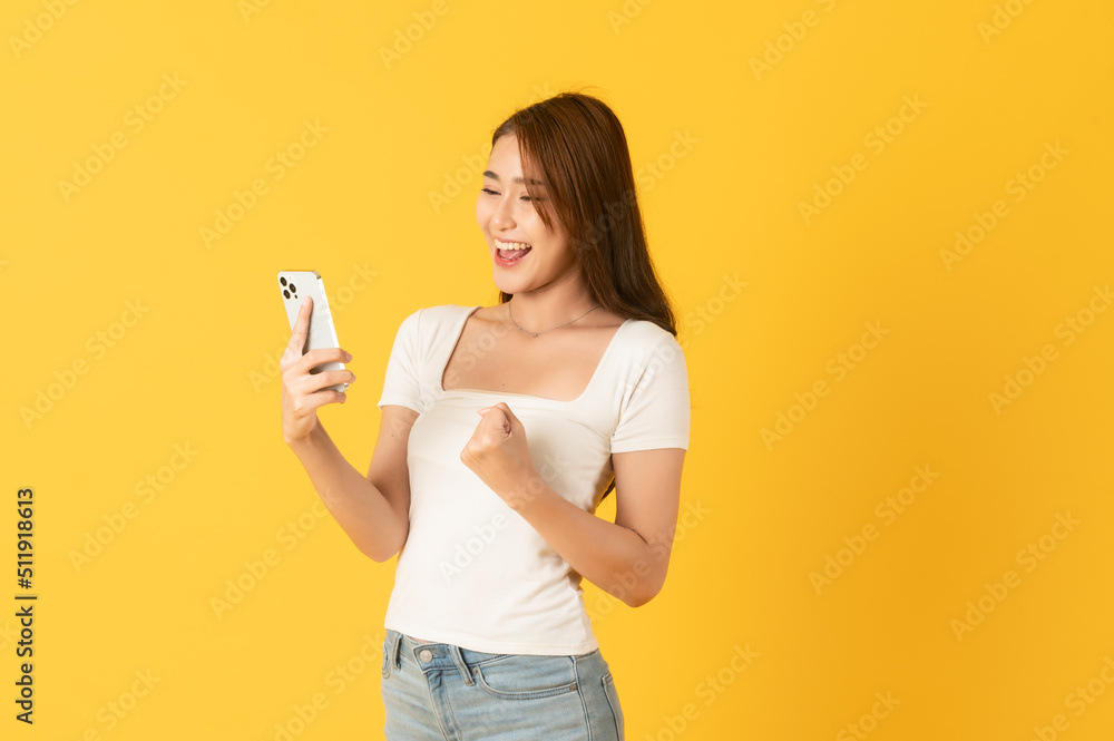 Surprise happy asian beautiful woman isolate on yellow background using smartphone Surprise happy asian beautiful woman isolate on yellow background using smartphone