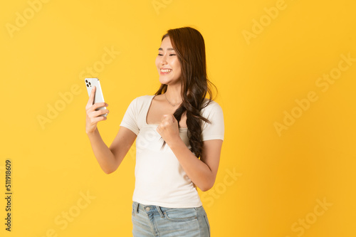 Surprise happy asian beautiful woman isolate on yellow background using smartphone