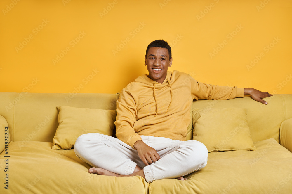 Happy mixed race man relaxing on the couch with yellow background Happy mixed race man relaxing on the couch with yellow background