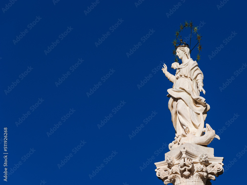 Statue of Virgin Mary of the Stars crushing dragon and crescent at the top of an ancient column in the historic center of Lucca, erected in 1687 (with blue sky and copy space)