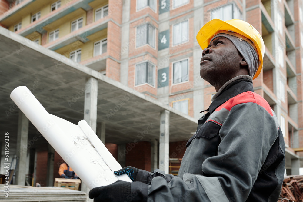 African American engineer in workwear looking upwards at highrise condo  while standing on construction area against building Stock Photo | Adobe  Stock